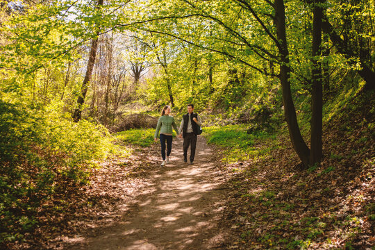 Couple walking leisurely on a sunlit forest path surrounded by lush greenery.