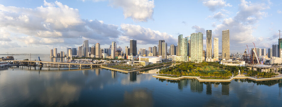 Aerial view of the city skyline reflecting on the water, with a bridge connecting to the mainland, and a vibrant park, Miami, Florida, United States.