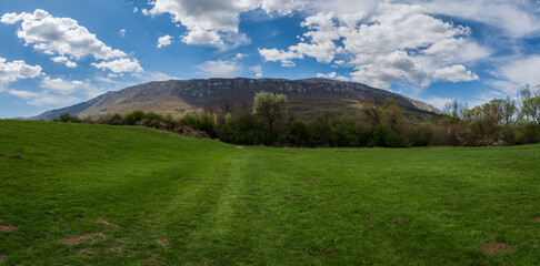 Amazing panorama of a green meadow in the mountains. The meadow is covered with a blue sky filled...