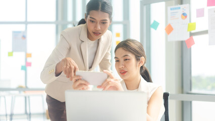 Two young adult business asian woman using smartphone girls talking gossip office news from social media