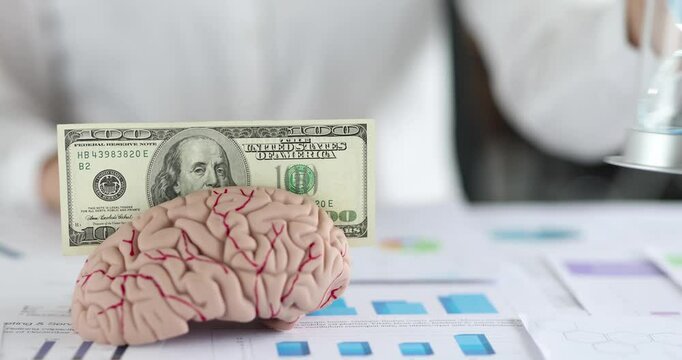 Female puts dollar on brain model putting hourglass creating symbolic contrast. Conceptual layout represents thinking value and limited time pressure