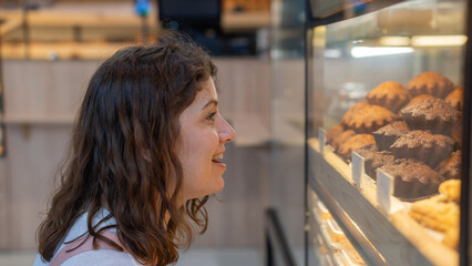 Caucasian woman looks greedily at baked goods in a bakery. 