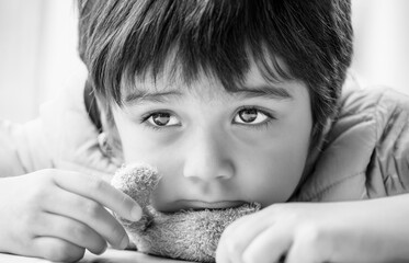 Black and White photo of kid face,Close up little boy looking out lying chin on teddy bear plush...