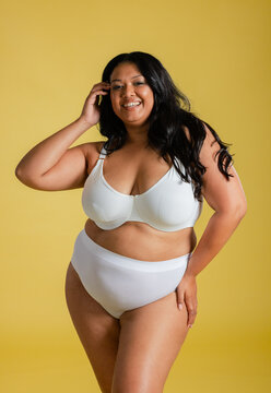 Woman modeling white underwire bra and high-waisted briefs against yellow backdrop in studio