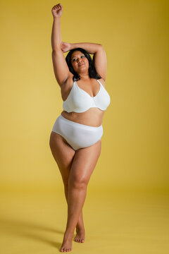 Woman stretching body dynamically on yellow seamless studio floor wearing white bra and briefs