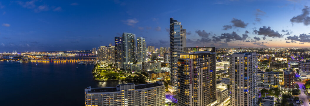 Aerial view of a city skyline reflecting the fading light of dusk over the water, with illuminated buildings contrasting against the deepening blue sky, Miami, Florida, United States.