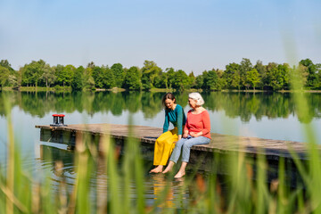 Mother and daughter sitting on a jetty by the lake enjoying a peaceful moment in nature