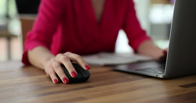 Female hand clicks computer wireless mouse completing tasks on laptop at desk. Office environment surrounds scene adding professional context