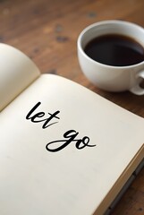 Inspirational words, Let go, written in elegant script on an open notebook next to a cup of coffee, vertical composition. A calming image perfect for mindfulness and selfcare themes.