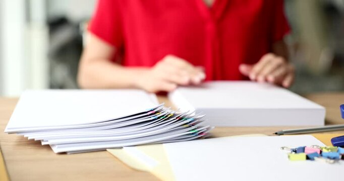 Woman makes stack of clean paper sheets preparing documents in light office. Female secretary engages in paperwork sitting at wooden desk