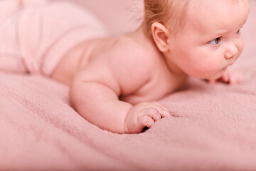 Young female child with light hair crawls on pink surface, eyes wide with curiosity. Soft natural...