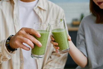 Two people toasting with green smoothies indoors