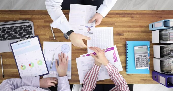 Office team meets around desk exchanging handshake above signed contract forms. Fingers lock in gesture creating moment of confirmed cooperation