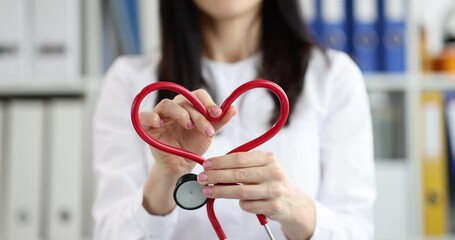 Woman doctor hands make heart of red stethoscope in clinic. Female cardiologist shows support to patients recovering from disease in hospital - Powered by Adobe