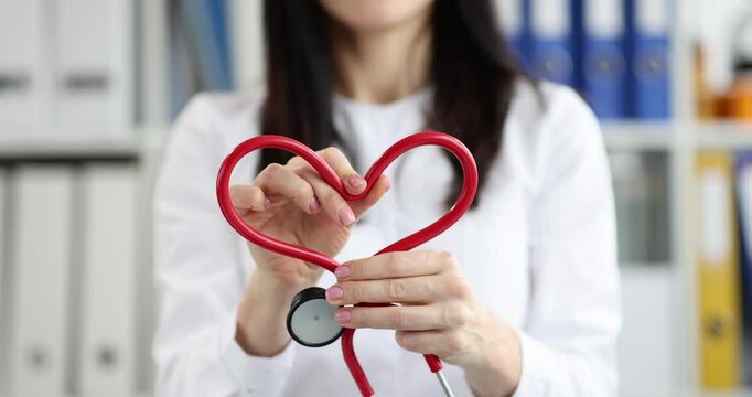 Woman doctor hands make heart of red stethoscope in clinic. Female cardiologist shows support to patients recovering from disease in hospital - Powered by Adobe