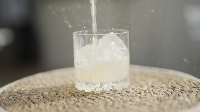 A glass of ice water sits on a rug. The glass is half full and the ice cubes are floating in the water. The scene is calm and peaceful, with the ice cubes adding a touch of coolness to the warm water