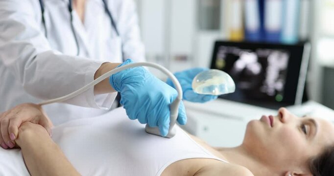 Doctor scans woman breast implants with ultrasound equipment in clinic. Female patient undergoes chest checkup with medical specialist in hospital