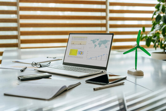 Office desk with laptop displaying charts and a small wind turbine model - Powered by Adobe