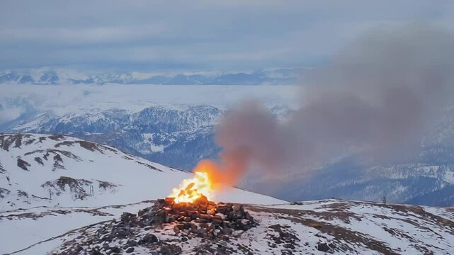Signal fire burning on snowy mountain top with scenic winter landscape
