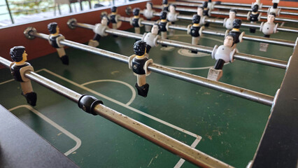 Rustic foosball table featuring worn-out rods and player figures in black and white, set on a green...
