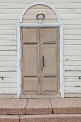 Old light brown wooden double doors with white arch and frame on light yellow wooden wall.