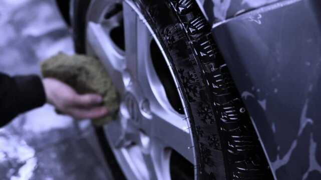 Man cleaning car wheel with sponge at car wash