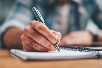 A man is writing in a notebook with a pen