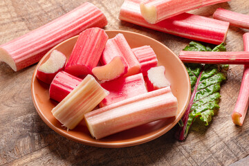 Cuts of red rhubarb stem on wooden plate on the table, top view.