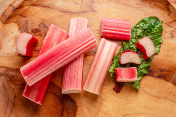 Cuts of red rhubarb stem on wooden plate on the table, top view.