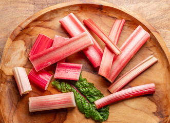 Cuts of red rhubarb stem on wooden plate on the table, top view.