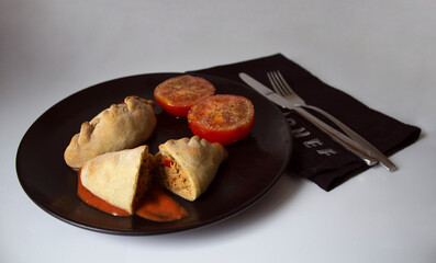 Delicious tuna pie, accompanied by a tomato split, with olive oil and oregano, stuffed with hard-boiled egg, bell pepper and olives.