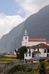 A white church with a pointed steeple stands before a towering mountain