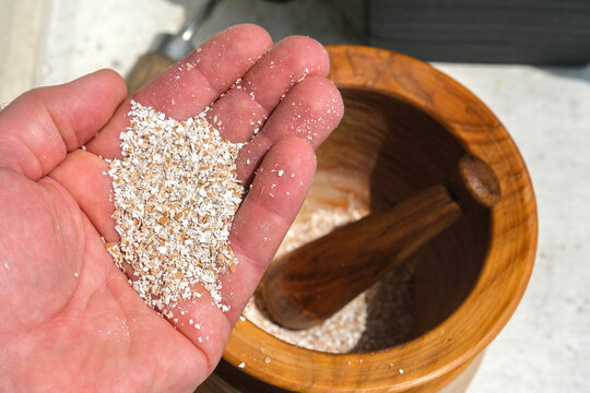 A hand crushes eggshells with a wooden pestle in a mortar, turning them into natural fertilizer for potted plants, eco-friendly and practical.