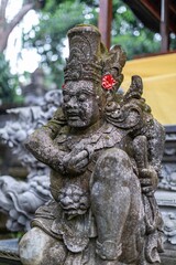 Balinese statue of a mythical guardian, adorned with a red flower, stands watch at a temple in...