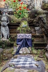 A Balinese Hindu shrine, adorned with traditional cloth, stands amidst moss-covered stone carvings and lush greenery in Ubud, Bali, Indonesia. The shrine is a place of worship.