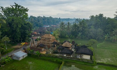 Aerial view of a Balinese Hindu temple under construction in Ubud, Bali, Indonesia. Workers are rebuilding the temple, surrounded by rice paddies.