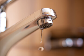 Dripping tap with water droplets inside apartment bathroom. Macro, close up, looking up shot,...