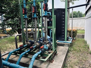 Water pump system with blue PVC piping and black storage tank in an outdoor industrial setting. Pressure gauges and motor pumps installed for fluid distribution and process efficiency.