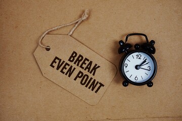 Break Even Point text on price tag with alarm clock on cork board background