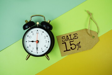 Sale 15% text on price tag with alarm clock and trolley shopping cart on green, yellow geometric...