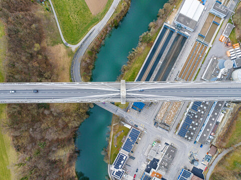 Aerial view of the Pont de la Poya bridge stretching over the meandering turquoise river, juxtaposed against the industrial landscape, Fribourg, Fribourg, Switzerland.