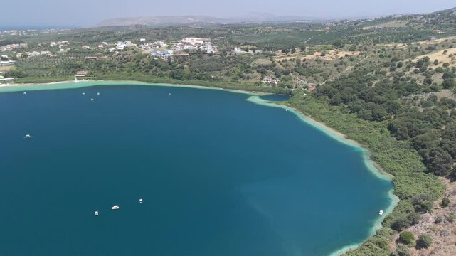 Fly with me above the Crete kournas lake during summer vacation phase with blue sky and sunshine while tourists use their paddle boat at the fresh sweet water lake