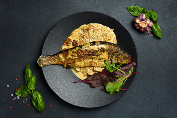 Baked trout fish with mushroom sauce. On a black round plate. Top view. Close-up.