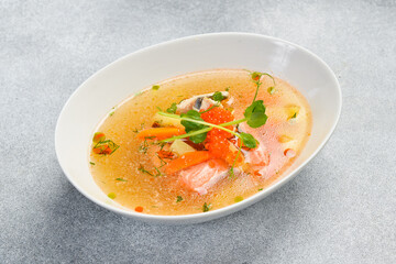 Seafood soup: salmon, sea bass with red caviar. In a white oval bowl. Close-up. Food rich in omega...