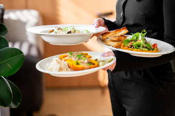 Restaurant server in black uniform holding three plates with fresh salad, creamy pasta, and...