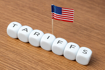 Cubes spelling "TARIFFS" are arranged in a line with a small American flag. Concept of tariffs, particularly in relation to the United States.