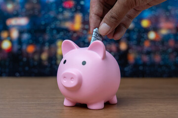 A hand is inserting a folded dollar bill into a piggy bank. Finance, saving money concept.