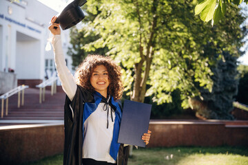 Achievement in life, with diploma. Cheerful graduate student in a gown is standing outdoors
