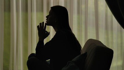 Silhouette of a distressed woman in front of backlit curtains