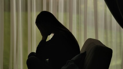 Silhouette of a distressed woman in front of backlit curtains